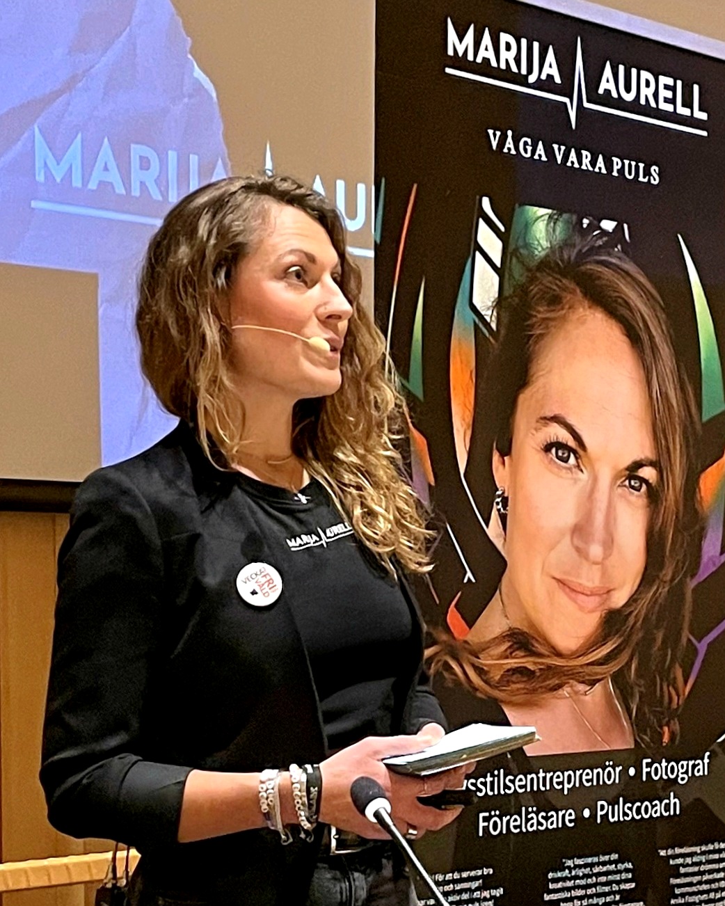 Marija talar med mikrofon i hörnet och vänder sig mot åhörarna